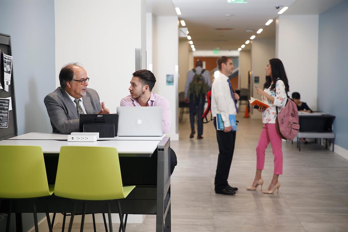 A student studies with a professor while other students walk in the hallway 