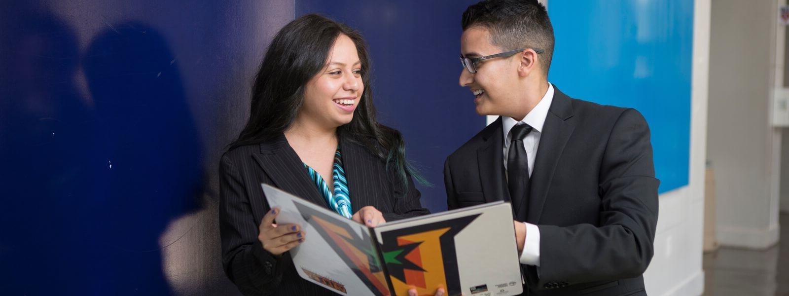 Two students in professional attire smiling at each other